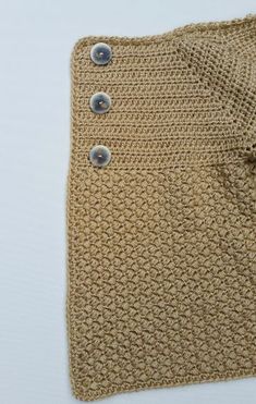 a crocheted sweater with buttons on the front and bottom, sitting on a white surface