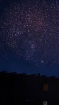 fireworks are lit up in the night sky above a building with windows and shutters