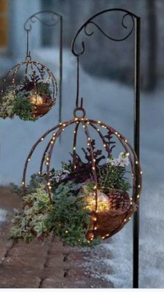 two christmas balls with lights hanging from them on a pole next to snow covered ground