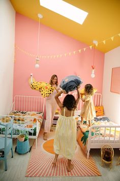 three girls in a room with pink walls and yellow accents, one holding an umbrella