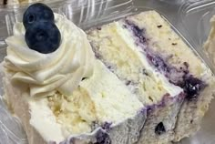 a piece of cake with white frosting and blueberries on top in a plastic container