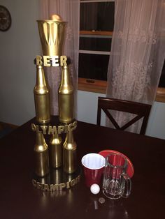 there are three gold bottles on top of each other and two cups in front of them