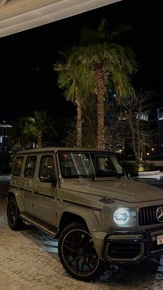 a mercedes g - class is parked in front of a building at night with palm trees