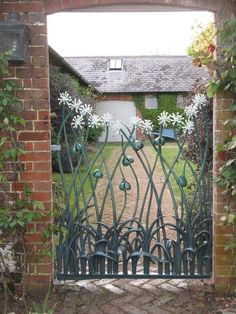 an iron gate with white flowers on it in front of a brick wall and house