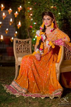 a woman sitting on top of a wooden bench wearing an orange and yellow sari