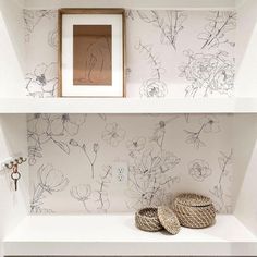 two baskets sit on top of a shelf in front of a wallpapered wall