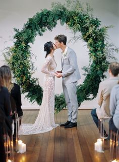 a newly married couple kissing in front of a green wreath with candles on the floor