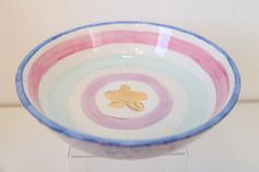 a colorful bowl with a gold fish in the center on a clear stand against a white wall