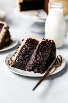 two slices of chocolate cake on white plates with milk and spoons next to them