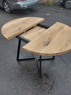 a wooden table sitting on top of a parking lot next to a silver car in the background