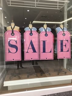 three pink sale signs are on display in a store window with mannequins