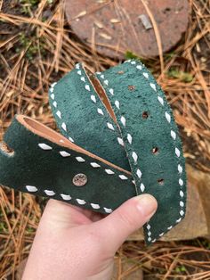 a hand holding a piece of green leather with white stitching on the outside and inside