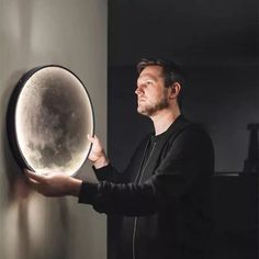 a man holding up a large mirror in his right hand and looking at it on the wall