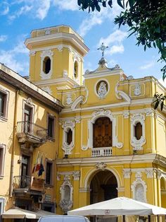 an old yellow building with a clock on it's side and people walking around