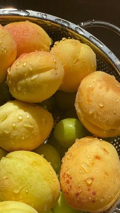 some green and yellow fruits in a metal bowl with water droplets on it's surface