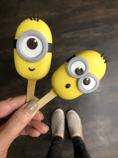 two yellow and black toy characters are on a wooden stick in front of someone's feet