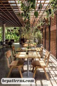 an outdoor dining area with wooden tables and chairs, surrounded by greenery on the walls