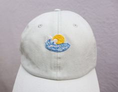 Hand Embroidered Light Blue,wave and sun hat. The perfect addition to your Spring/Summer wardrobe this season, every design is hand drawn and hand embroidered onto the hat meaning that each one is individually unique. 🌿 Perfect for everyday wear or makes a great gift. 🌿 One size fits all with an adjustable buckle on the back. 🌿 The cap is 100% cotton embroidered with cotton thread. 🌿 Care instructions - Hand wash warm 30oC. ** Please note that hat colours may differ slightly due to the lighting on the images ** If you would like additional details such as any measurements, or further customisation please don't hesitate to contact me. Other hats are available in my Etsy shop. Summer Hats With Embroidered Logo, Adjustable Summer Baseball Cap With Embroidered Logo, Summer Adjustable Baseball Cap With Embroidered Logo, White Embroidered Logo Dad Hat For Summer, Summer Embroidered Logo Baseball Cap, Summer Baseball Cap With Embroidered Logo And Curved Brim, Embroidered Logo Baseball Cap For Summer, White Dad Hat With Embroidered Logo For Summer, White Summer Hat With Embroidered Logo