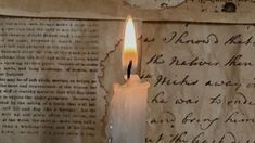 a lit candle sitting on top of an old book next to a piece of paper