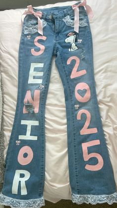 a pair of blue jeans with pink lettering on them sitting on a white bed next to a pillow