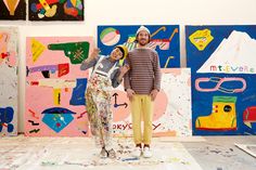 two people standing next to each other in front of paintings on the wall and floor