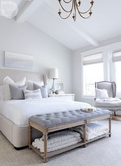 a large white bed sitting in a bedroom under a chandelier and two windows