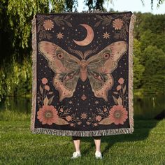 a woman standing in the grass holding up a blanket with a butterfly and moon on it