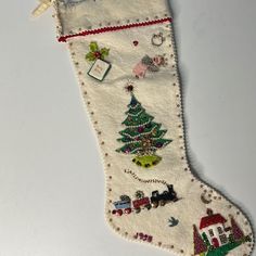 an embroidered christmas stocking hanging on a white table with a red ribbon around it