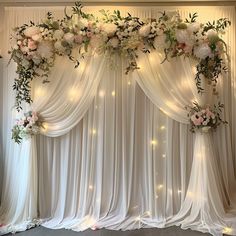 a white backdrop with flowers and greenery on the top, along with fairy lights