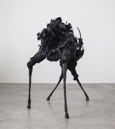 an animal made out of black paper on top of a cement floor next to a white wall