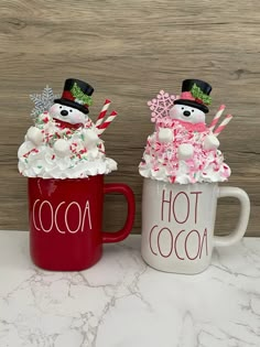 two coffee mugs decorated with marshmallows and candy canes in the shape of snowmen