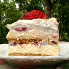 a piece of cake with strawberries on top is sitting on a plate in front of some trees