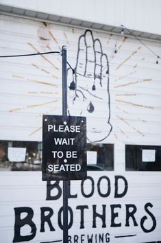 a sign that says please wait to be seated blood brothers brewing on the side of a building