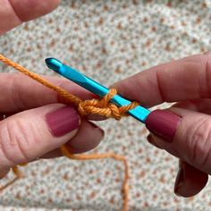 two hands holding crochet hooks with yarn in the foreground and an orange string on the other hand