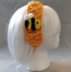 a crocheted hat with a bee on it's side, sitting on a mannequin head