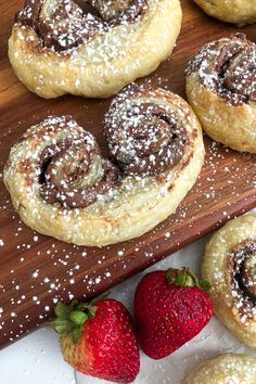 several pastries and strawberries sit on a wooden cutting board with powdered sugar