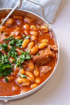 a bowl filled with beans and meat in tomato sauce on top of a white table