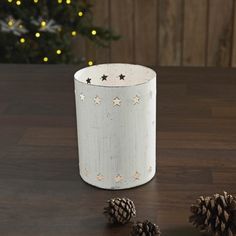 a white candle holder sitting on top of a wooden table next to two pine cones