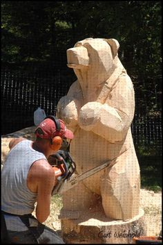 a man sanding next to a large bear statue with a sawduster in his hand