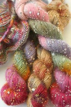 several skeins of colorful yarn are on a white surface with sequins