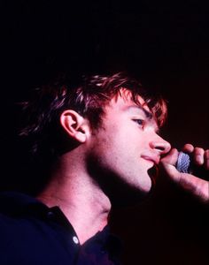 a young man holding a microphone up to his ear and singing into the microphone in front of him