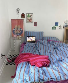 an unmade bed with blue and red striped comforter in a white walled room