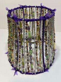 a close up of a bracelet on a white surface with purple ribbon and beads hanging from it