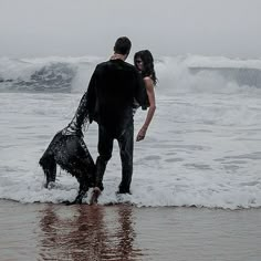 a man and woman standing in the surf with their dog