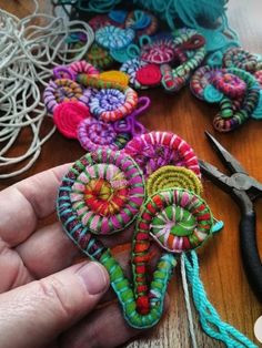 a person is holding some colorful items on a table next to scissors and thread spools