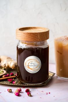 a glass jar filled with brown liquid next to a cup of coffee and cinnamon sticks