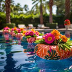 colorful flowers are in an orange vase on the edge of a swimming pool with palm trees behind it