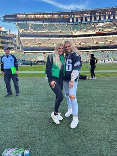 two women posing for the camera in front of an empty football field at a stadium