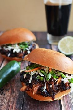 two pulled pork sandwiches with cole slaw on a wooden table next to a glass of beer