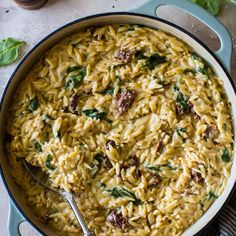 a pot filled with pasta and spinach on top of a table next to a spoon